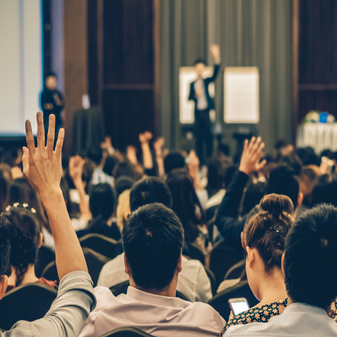 Audience raising hands during a speaker presentation supported by AV rentals for events